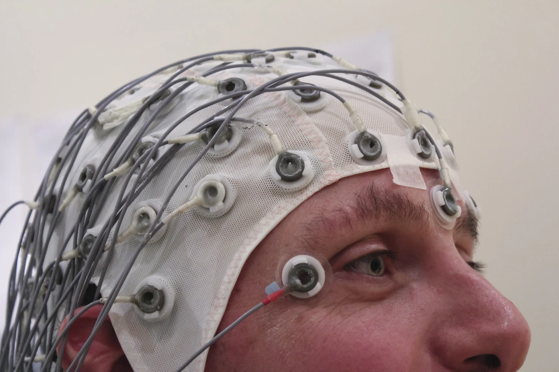 A person wears a cap fitted with many wired scalp electrodes.