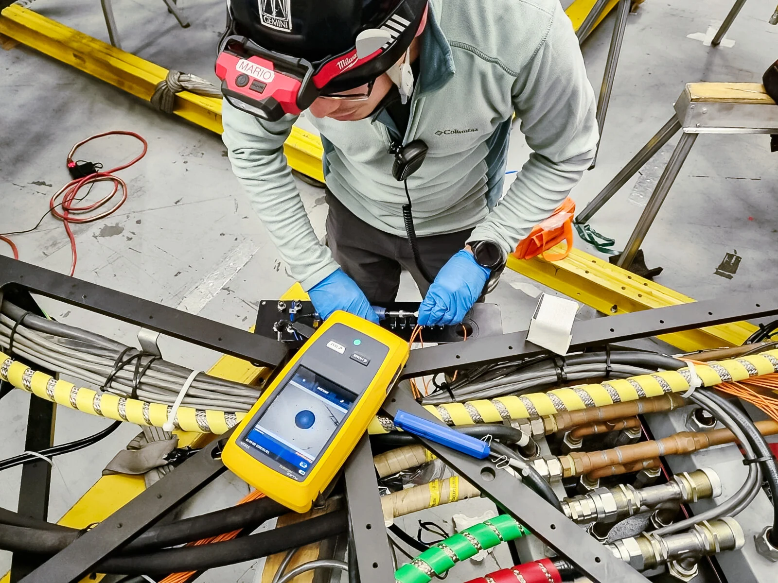 A technician checks fibre-optic connections beside a yellow test instrument.