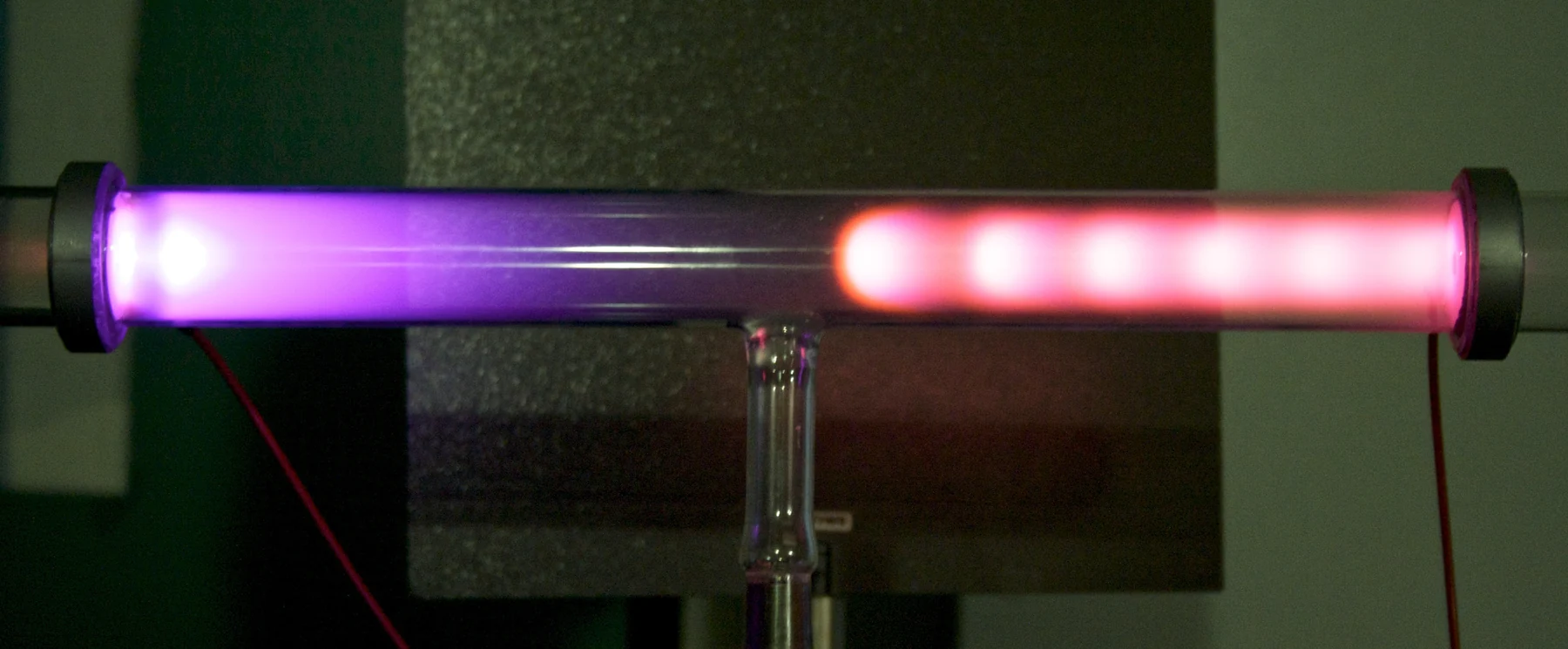 Pink and violet regions glow along a horizontal glass discharge tube.