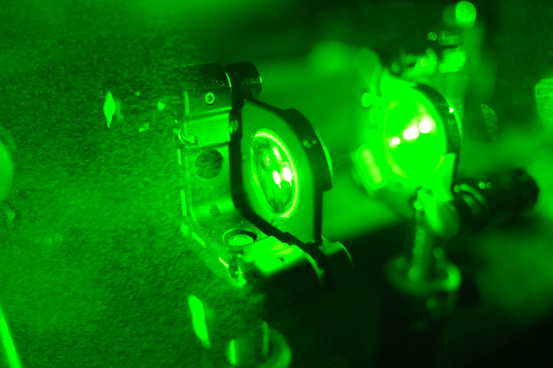 Green laser light passes through a lens assembly mounted on an optical table.