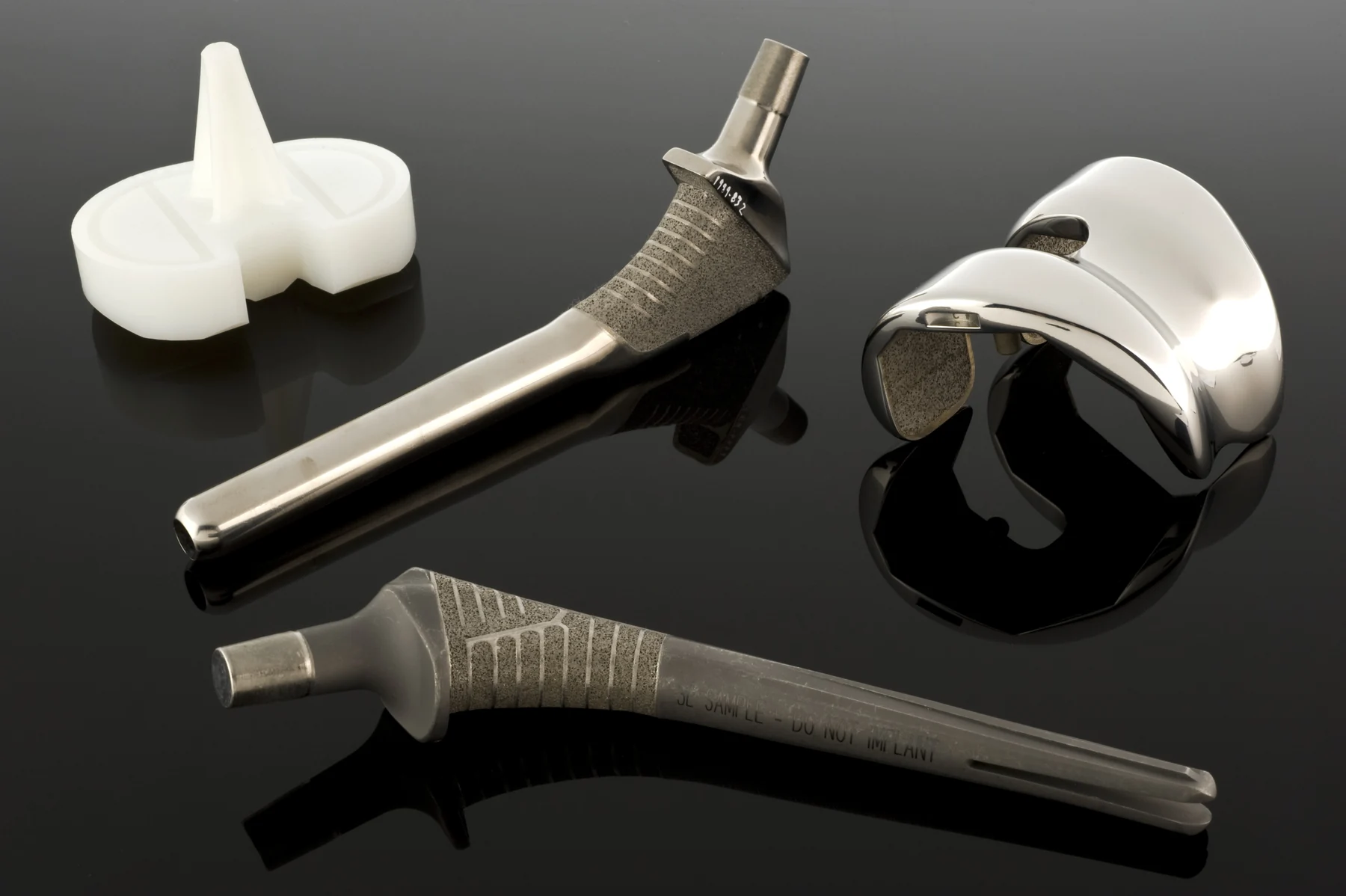 Metal and pale polymer hip-replacement components are arranged on a dark reflective surface.