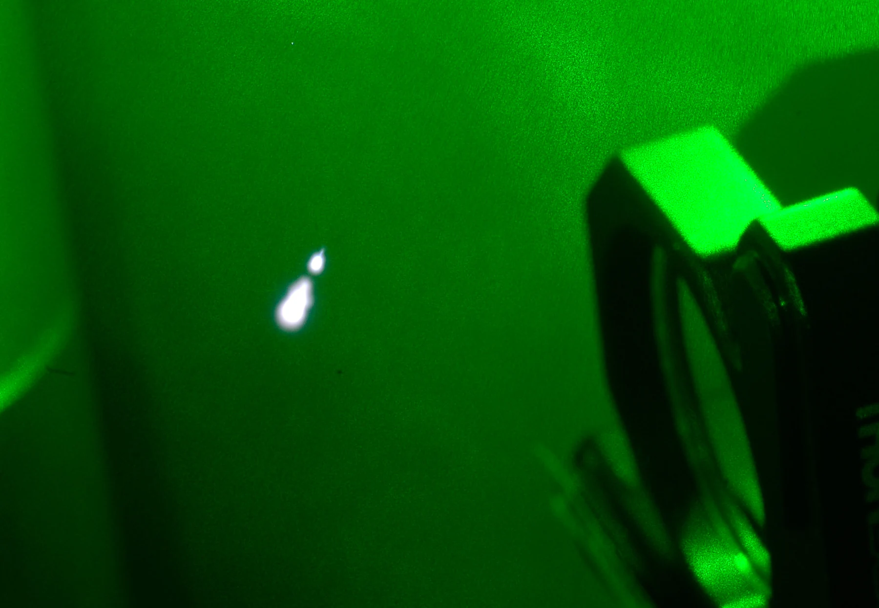 A bright point of plasma appears near a focusing lens in a green-lit optical experiment.