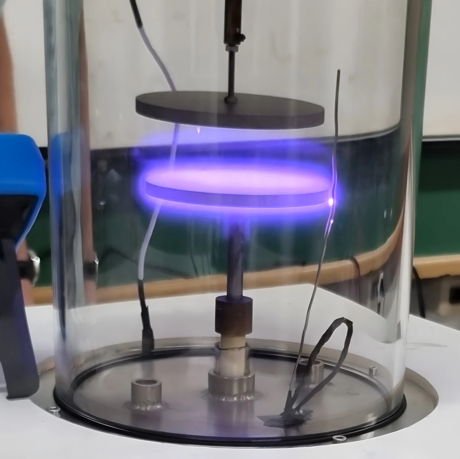 A violet ring of plasma glows between electrodes inside a transparent cylindrical chamber.