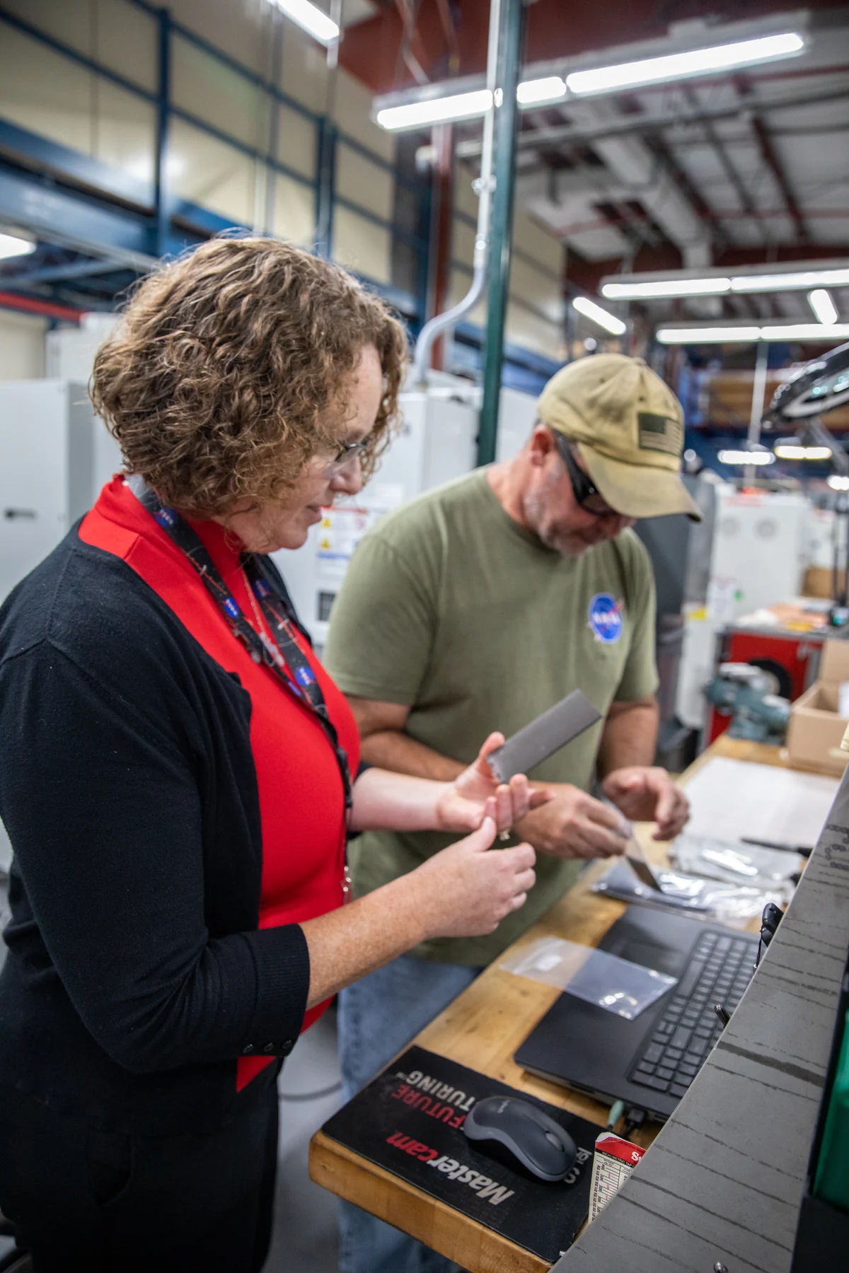 Two researchers inspect metallic samples on a workbench in a large laboratory.