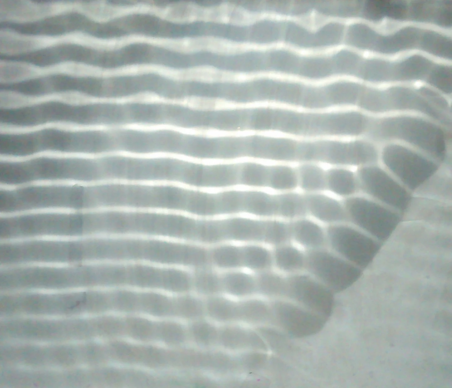 Bright and dark parallel ripple patterns curve across the surface of a shallow tank.
