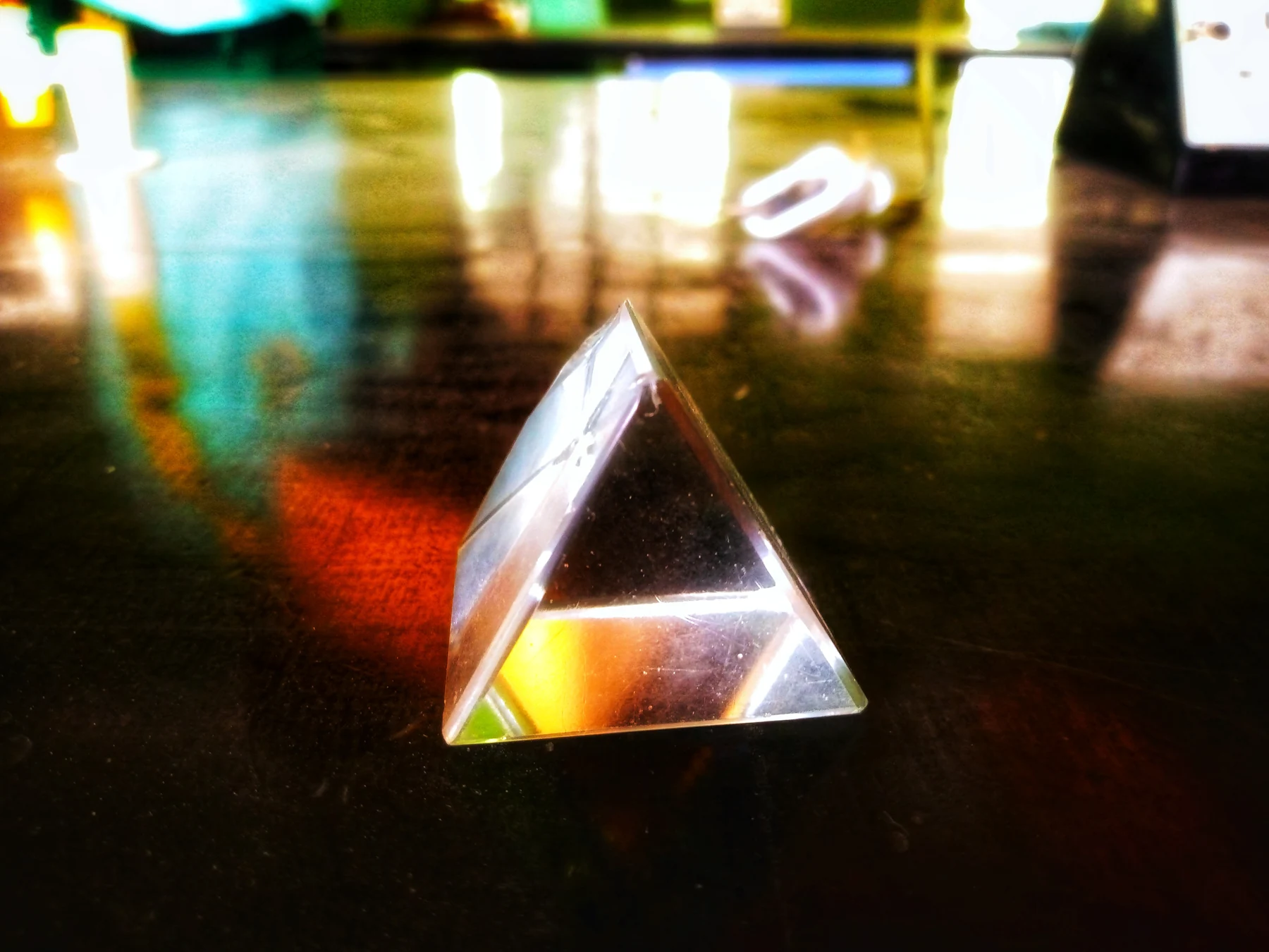 A small triangular glass prism refracts warm light on a dark reflective table.