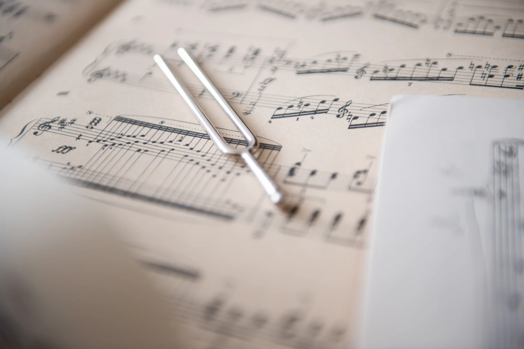 A metal tuning fork rests diagonally across a page of printed music.