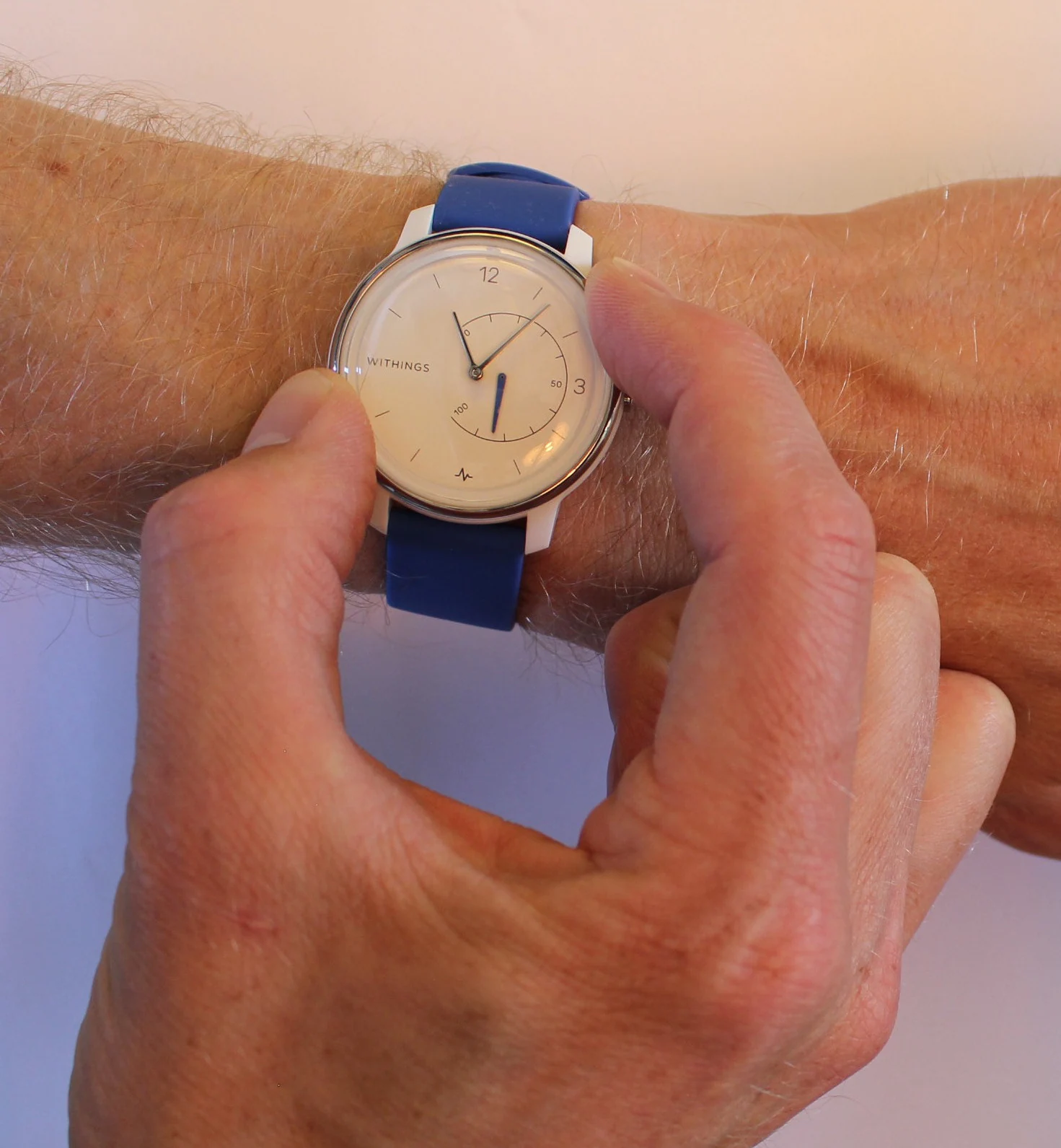 A person touches the side of a wristwatch while it is worn on the opposite arm.